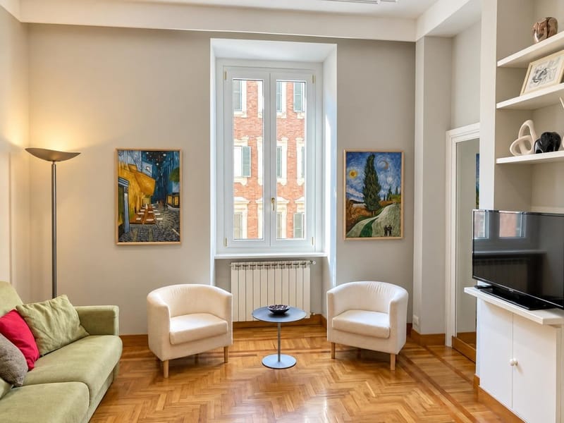 After: the same living room in warmer light with the floor lamp on; armchairs, pictures and window unchanged