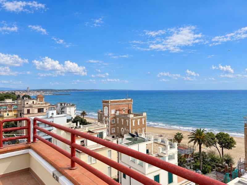 Después: vista al mar con cielo azul en lugar de gris, mar más azul, terraza despejada y edificios más luminosos.