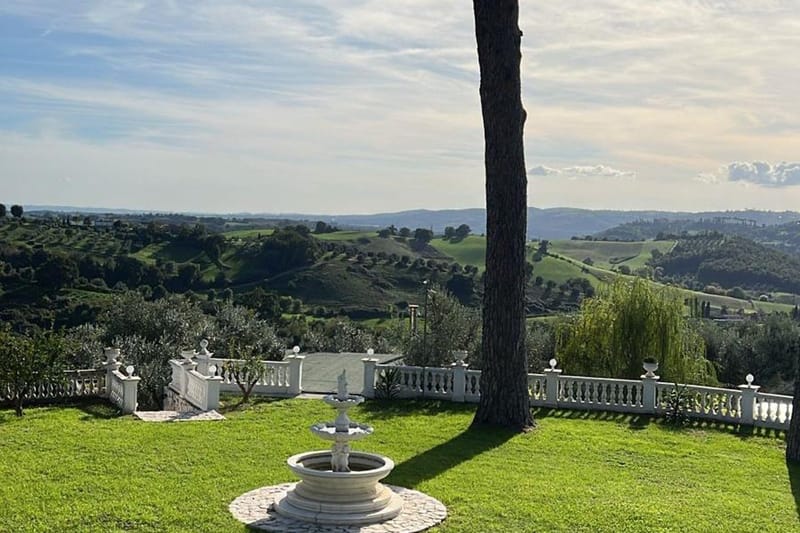 Before: garden with a fountain, a white balustrade and hills in the background under a pale, hazy sky